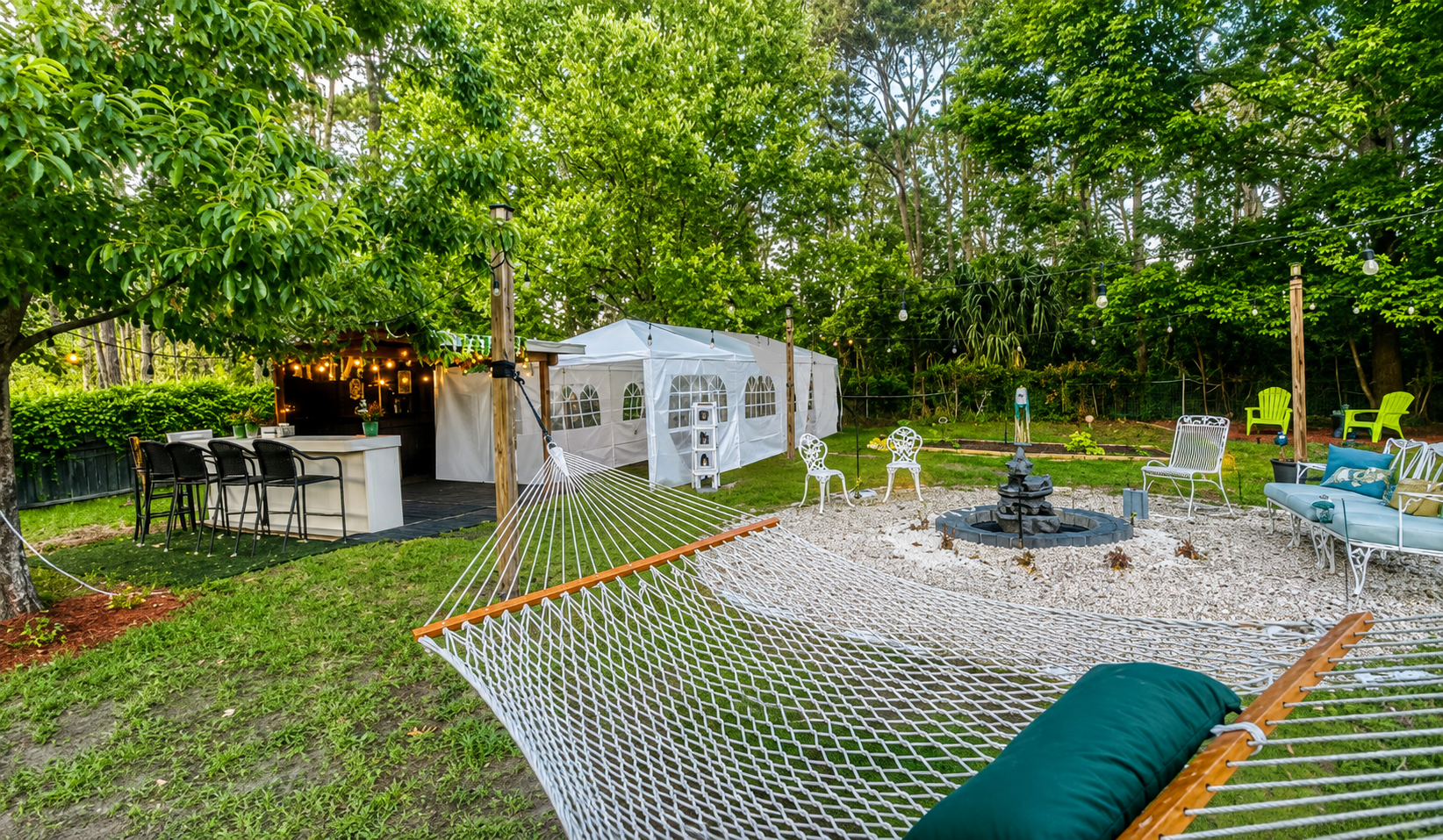 A hammock beside the Holy Acres tent, outdoor bar, fire feature, and garden seating